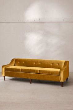 a yellow couch sitting on top of a cement floor next to a white brick wall