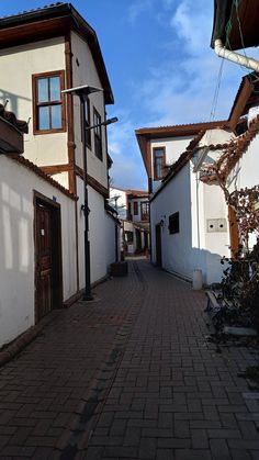 an alley way with white buildings and brown doors on both sides, surrounded by brick walkways