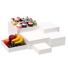 three white boxes filled with cupcakes, fruit and muffins sitting on top of each other