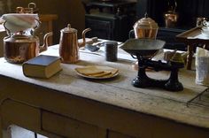 an old table with tea kettles, books and other items on it in front of a fireplace