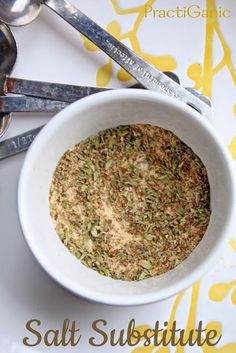 a white bowl filled with food next to spoons on top of a yellow and white table