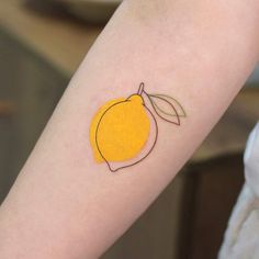 a small tattoo on the arm of a person with a yellow apple and green leaf