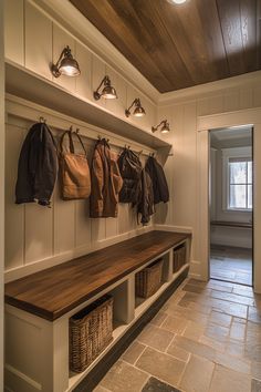 a wooden bench sitting next to a wall filled with purses and coats on hooks