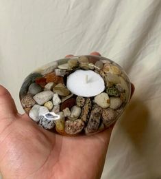 a hand holding a small candle surrounded by rocks