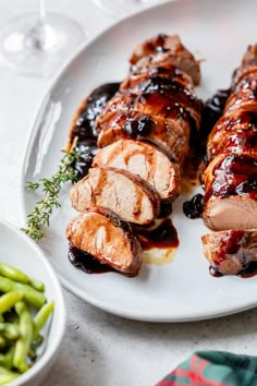 a white plate topped with meat covered in bbq sauce next to green beans and a glass of wine