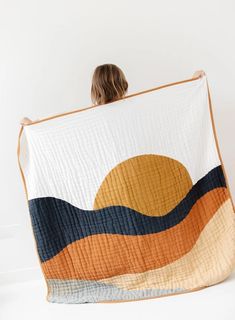 a woman is holding up a quilt that looks like an ocean wave with the sun in the background