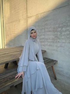 a woman sitting on top of a wooden bench wearing a hijab and dress