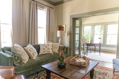 a living room with green couches and pillows on the coffee table in front of two windows