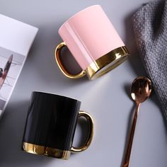 two coffee mugs sitting on top of a table next to a book and spoon