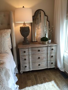 a bedroom with a dresser, mirror and lamp on it's side table in front of the bed