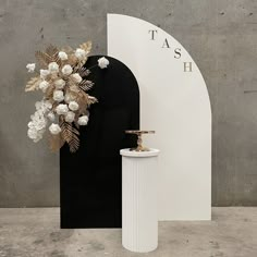 a tall white vase with flowers in it next to a black and white sign that says tash