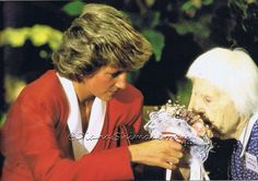 an older woman is handing something to another woman with flowers in her lap and holding the other hand