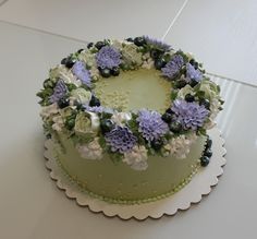 a green cake with white and blue flowers on the top is sitting on a table