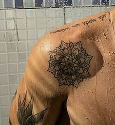 a man with tattoos on his back standing in front of a tiled wall and shower