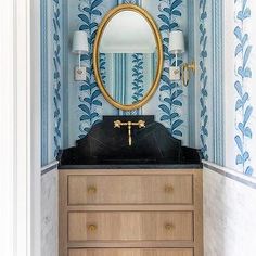 a bathroom with blue and white wallpaper, gold mirror and black countertop sink