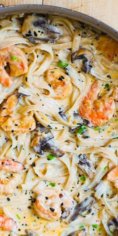 a pan filled with pasta and shrimp on top of a wooden table