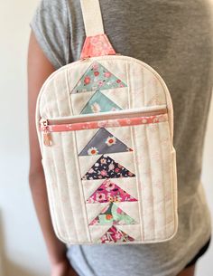 a woman is holding a white backpack with colorful triangles on it