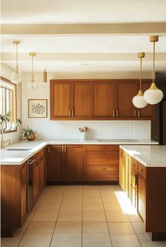 a kitchen with wooden cabinets and white counter tops, two hanging lights above the sink