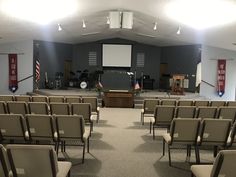 an empty auditorium with rows of chairs in front of a podium and projector screen