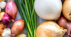 an assortment of vegetables including onions, leeks and garlic on a gray table top