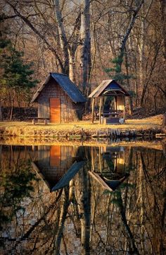 an old cabin sits on the edge of a lake surrounded by trees and leaves, with its reflection in the water