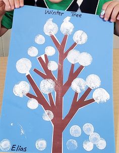 a young boy holding up a paper cut out of a tree with snow on it