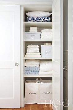 an organized closet with white linens and storage bins on the bottom shelf in front of it