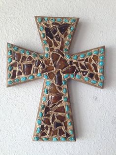 a wooden cross with blue and brown stones on it's sides hanging from the wall