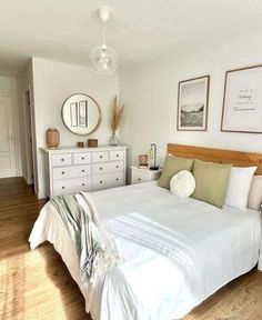 a bedroom with white walls and wooden floors has a bed, dressers, and pictures on the wall