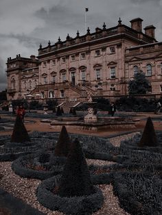 an old building with many bushes in front of it and a fountain on the ground