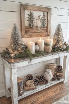 a table with candles and pine cones on it in front of a framed picture frame