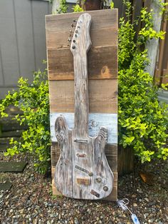 a wooden guitar sitting on top of a pile of rocks next to a planter