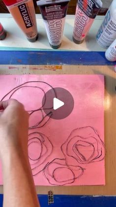 someone is drawing roses on a piece of pink paper with markers and paintbrushes