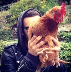 a man holding a chicken in his hands while wearing a black jacket and hoodie