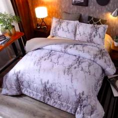 a bed with white and grey marbled comforter on top of it next to a night stand