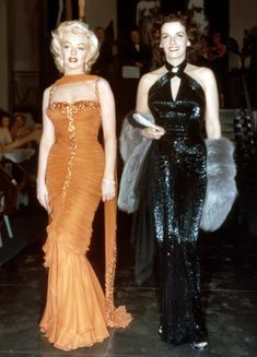 two women in evening dresses walking down a runway