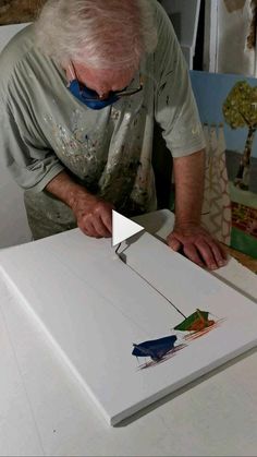 an older man is working on some art work with scissors and glue, while looking down at the paper