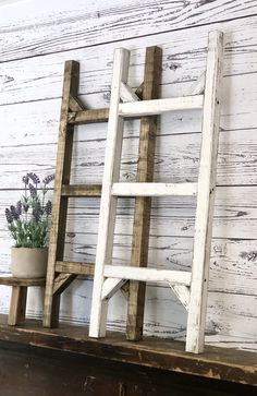 an old wooden ladder leaning against a white painted wall next to a potted plant