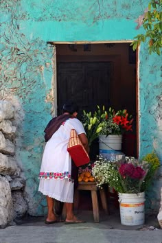 a woman standing in front of a blue building with potted plants and flowers on display