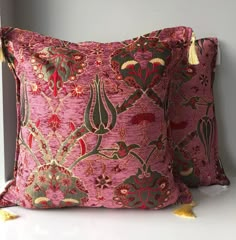 two pink and green pillows with tassels on them sitting next to each other