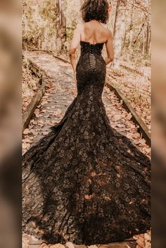 a woman in a black dress is walking through the woods with her back to the camera