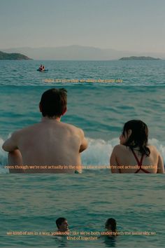 two people sitting in the ocean watching another person swim