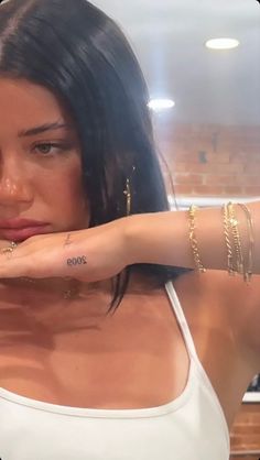 a woman with tattoos on her arm posing for a photo in the kitchen, wearing gold bracelets and a white tank top