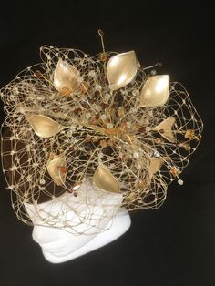 Delicate gold fascinator perfect for the guest who wants something fairly understated. This design is a beautiful selection of glass effect leaves and flowers with an additional scatter of brown crystal and tan glacier stone, clustered together amongst a fine layer of veiling and set onto a fine comfort base tiara band. As with all our designs, this piece can be made exact to the image or in any colour combination to match in with your outfit. If a specific colour is required customers can messa Handmade Gold Hat For Kentucky Derby, Elegant Fascinator For Celebrations, Elegant Handmade Headpiece With Structured Crown, Elegant Cream Headpiece For Gift, Handmade Gold Hair Accessories For Wedding, Elegant Handmade Fascinator With Pinched Crown, Evening Headpiece With Handmade Flowers And Pinched Crown, Elegant Headpiece With Handmade Flowers, Gold Hat With Structured Crown For Party