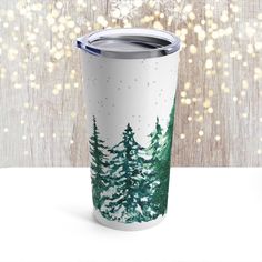 a white and green tumbler cup with trees painted on it, surrounded by lights