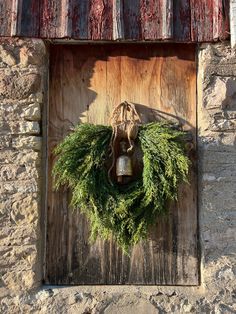 a wreath is hanging on the side of a wooden door with a bell in it