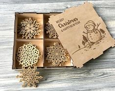 four wooden snowflakes in a box on top of a wood table next to a card