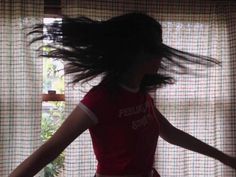 a woman with her hair flying in the air next to a sheered window curtain