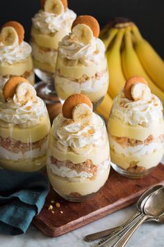 several desserts with bananas and whipped cream on a wooden tray next to silverware