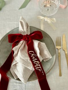 a table setting with napkins, silverware and red ribbon tied around the place settings